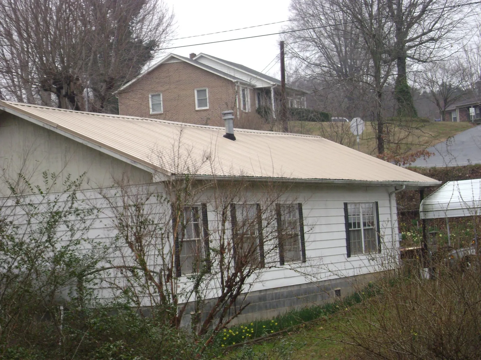 Tan metal roof on a white sided house set into a hillside — Commercial Roofing by Roofing Brothers in Bristow